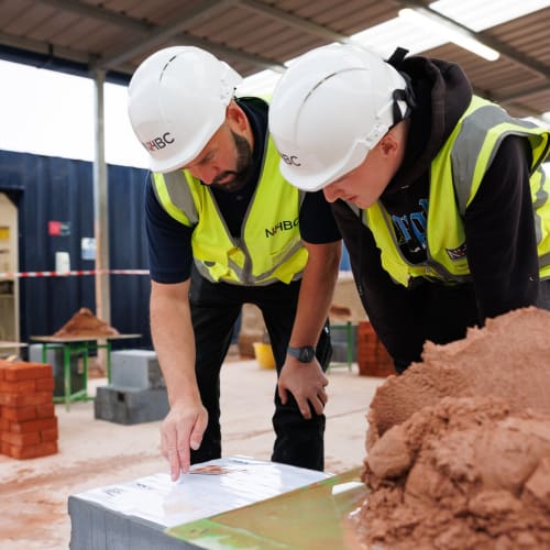 An apprentice and tutor in full ppe looking at a document