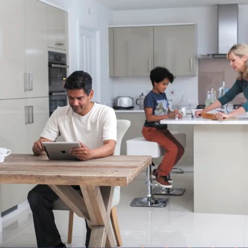 Family in modern kitchen with man at table with ipad