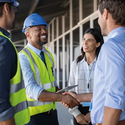 Team on site with safety jackets and hard hats shaking hands