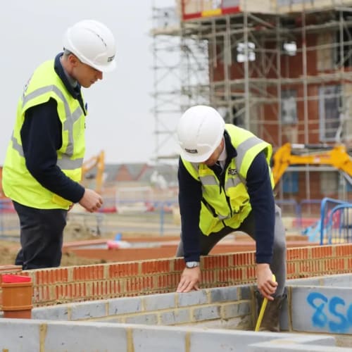 Two men in safety jackets and hard hards on new home development site looking at brick level