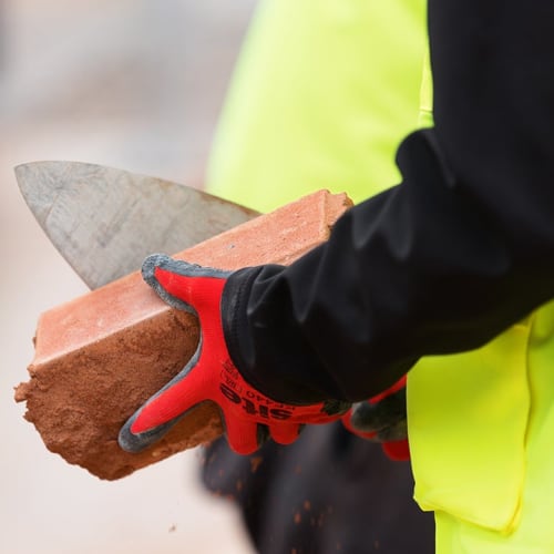 a hand in a red glove holding a brick with a trowel