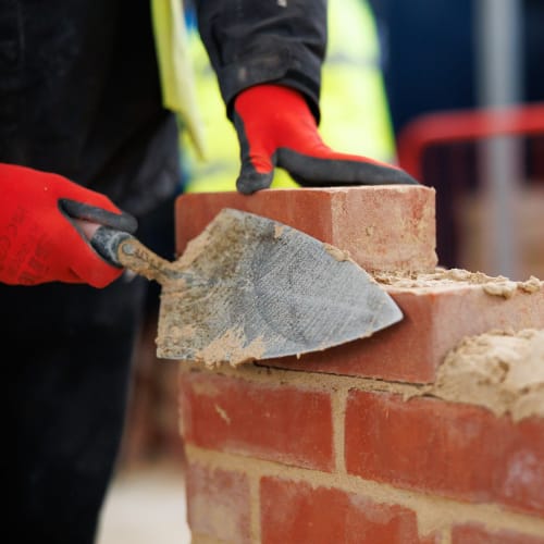 an apprentice in gloves with a trowel laying bricks