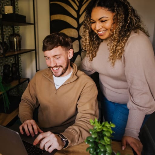 Couple smile at laptop in new build home