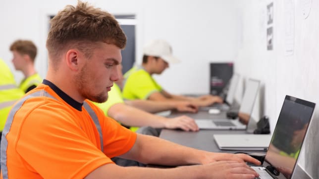 An apprentice in orange PPE on a laptop