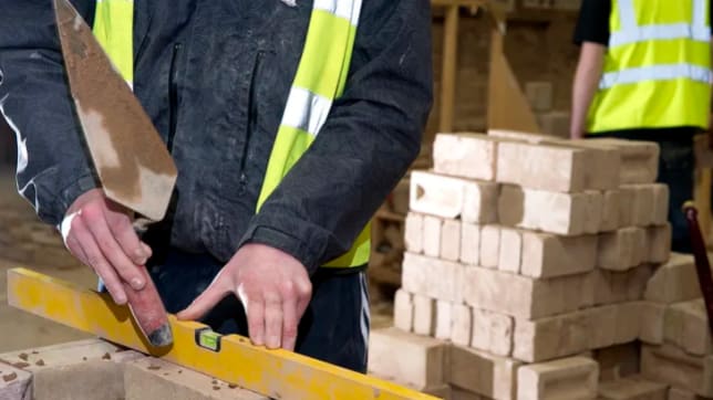 Man with safety jacket and spirit level on wall