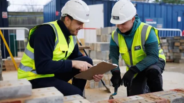two people in hi-vis jackets and hard hats looking at a clipboard
