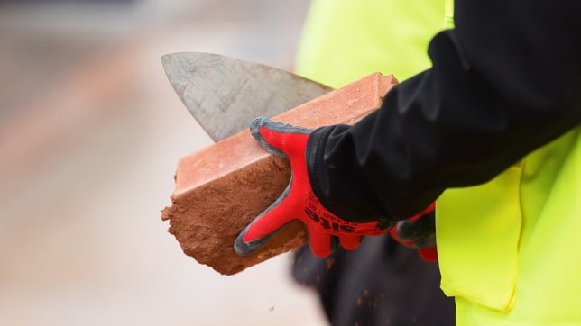 a hand in a red glove holding a brick with a trowel