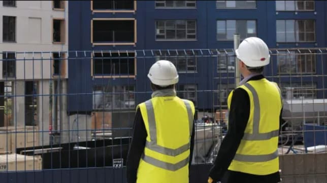 People in safety jackets and hard hat looking at building