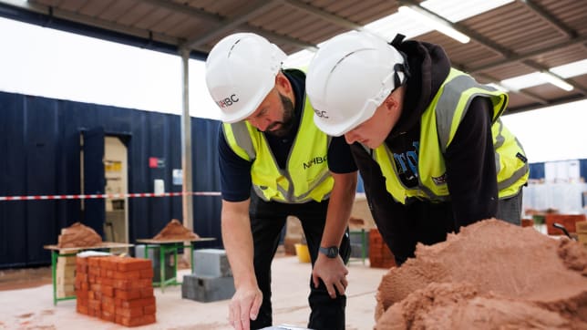 An apprentice and tutor in full ppe looking at a document
