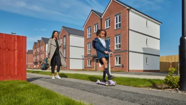 Woman and child walking past new build homes on sunny day