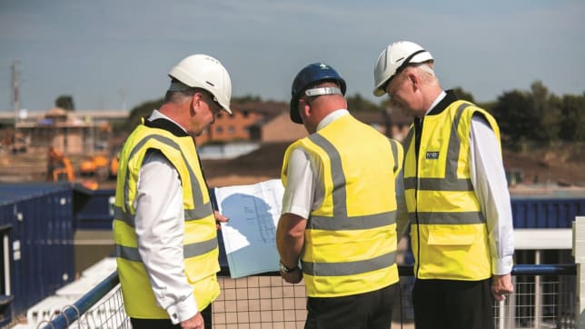 Three men in safety jackets and hard hats looking at home details on site