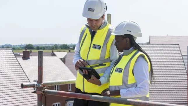 Team in NHBC safety jackets and hard hats on roof looking at pad.