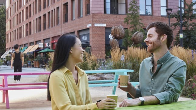 Two people drinking a coffee on a picnic bench