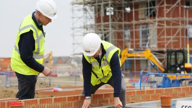 Two men in safety jackets and hard hards on new home development site looking at brick level