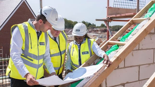 Three NHBC builders in high vis study housing blueprints on a construction site