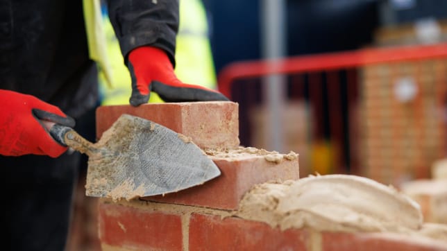 an apprentice in gloves with a trowel laying bricks