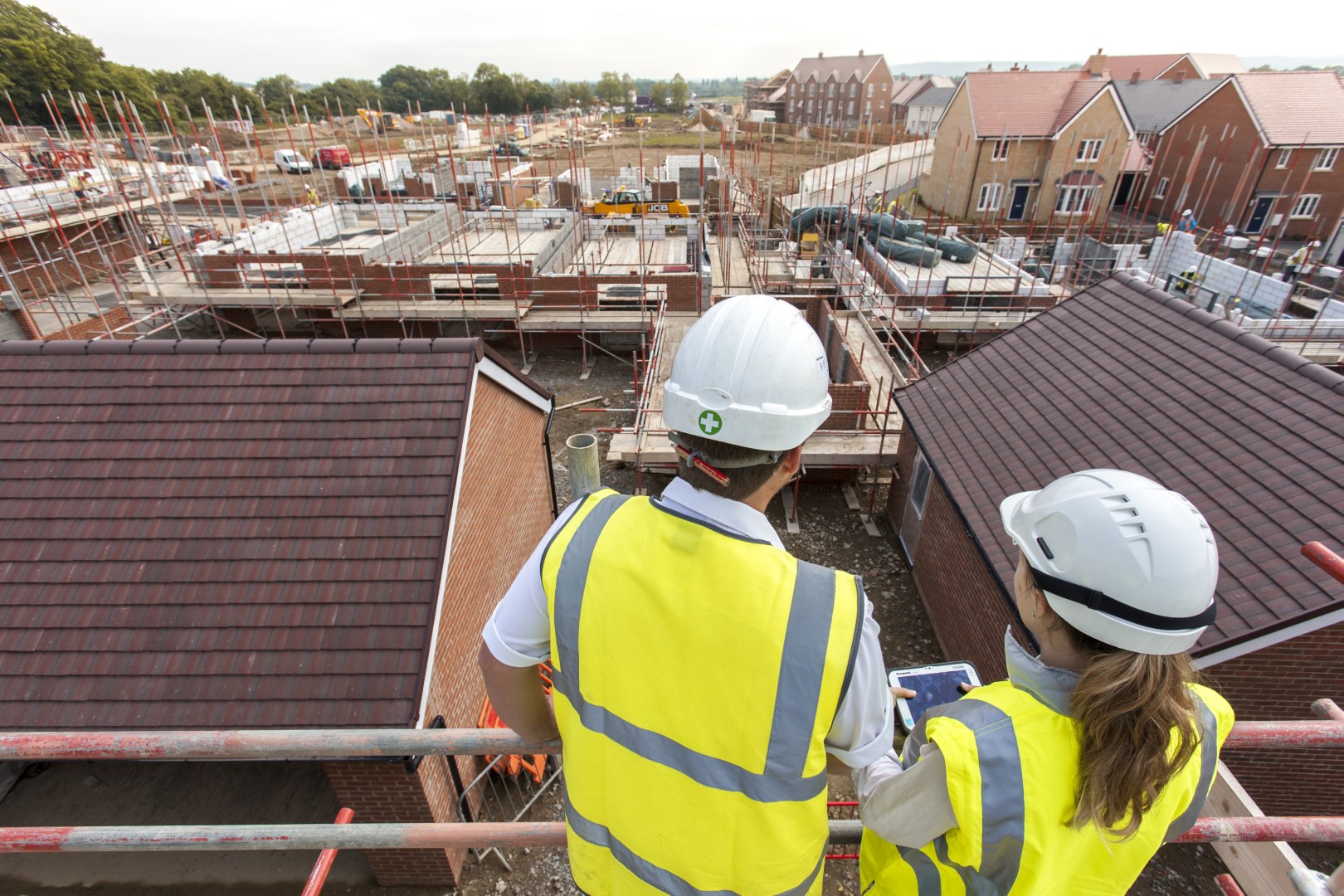 two people in site safety clothing standing on scaffolding while looking at the development