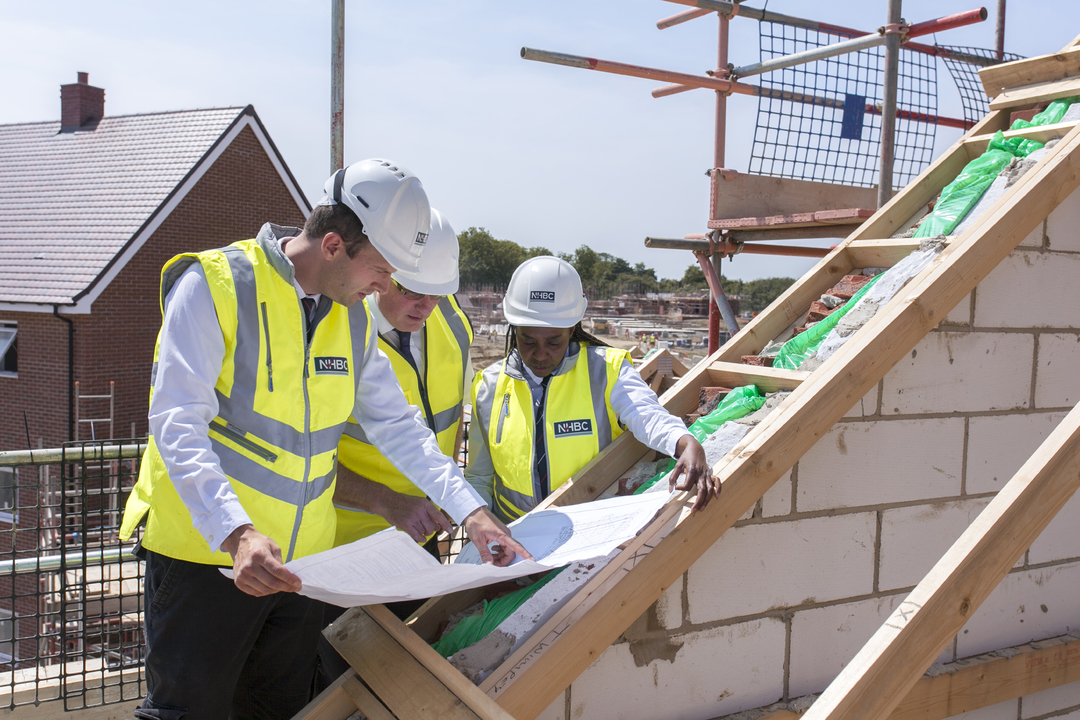 people in site safety clothing and hard hats standing on scaffolding while looking at plans