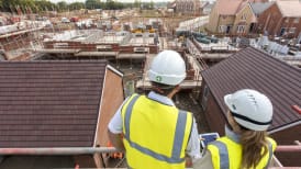 two people in site safety clothing standing on scaffolding while looking at the development