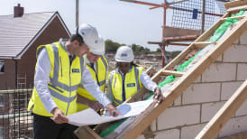 people in site safety clothing and hard hats standing on scaffolding while looking at plans