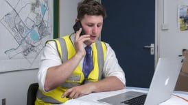 a guy wearing site safety clothing sitting in an office talking on the phone