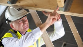 a man in site safety clothing investigating a metal joist on a wooden beam