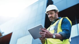 a man in site safety clothing and a hard hat looking at a tablet