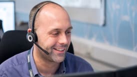 man sitting at his desk and smilinghile wearing a headset