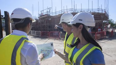 two men and a woman wearing high vis jackets and hard hats looking at building plans