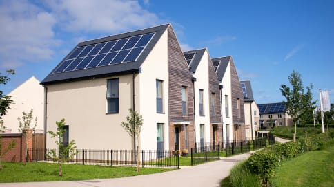 wooden and white houses with solar panels on the roof below a blue sky