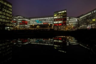 Nighttime view of modern office buildings with colorful illuminated windows reflecting in a still body of water
