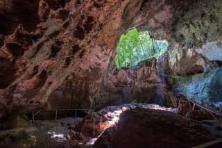 A large cave with jagged rock formations and a clear opening at the top, allowing sunlight to illuminate the interior.