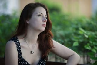 A woman with long hair wearing a polka dot dress gazing off to the side with greenery in the background.