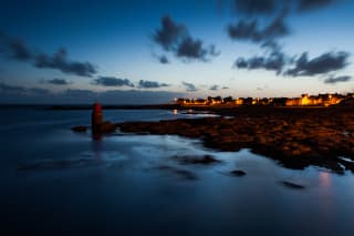 Photo of the Atlantic coast at Guilvinec, with rocks uncovered at low tide, and glimmers of the town in the distance.