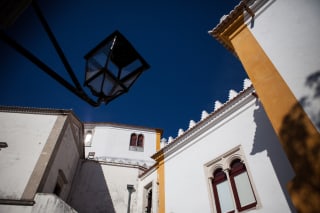 White traditional buildings with ornate edges against a clear blue sky, featuring a street lamp in the foreground.