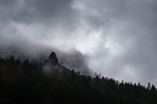 Mountain peaks shrouded in mist with a dark forest in the foreground.