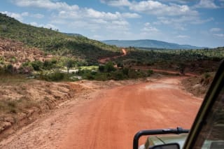 Photo of a red dirt track making turns in hills covered with low vegetation