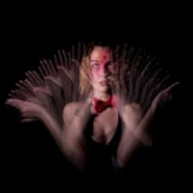 Bust picture of a young woman moving back and forth with her arms, visible in several places thanks to the light of a stroboscope.
