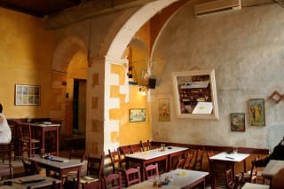 Interior of a rustic cafe with arched doorways, wooden tables and chairs, warm yellow walls, and several vintage framed pictures.