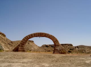 Brick archway standing in a desert landscape with clear skies.