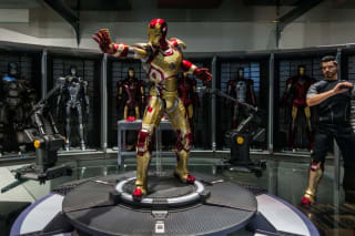 Iron Man suit on display with other suits in the background and a figure resembling Tony Stark to the side.