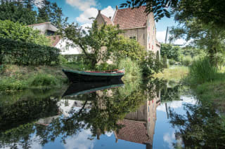 Photo of a boat on a canal, with houses in the background, all reflected in the water