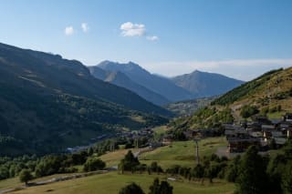A picturesque mountain valley with lush greenery, scattered wooden houses, and a winding road.