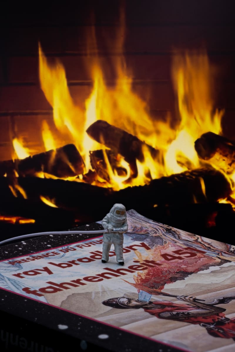 Photo of a miniature firefighter in a fireproof suit on the cover of the book Farenheit 451 by Ray Bradbury, with a fire in the background
