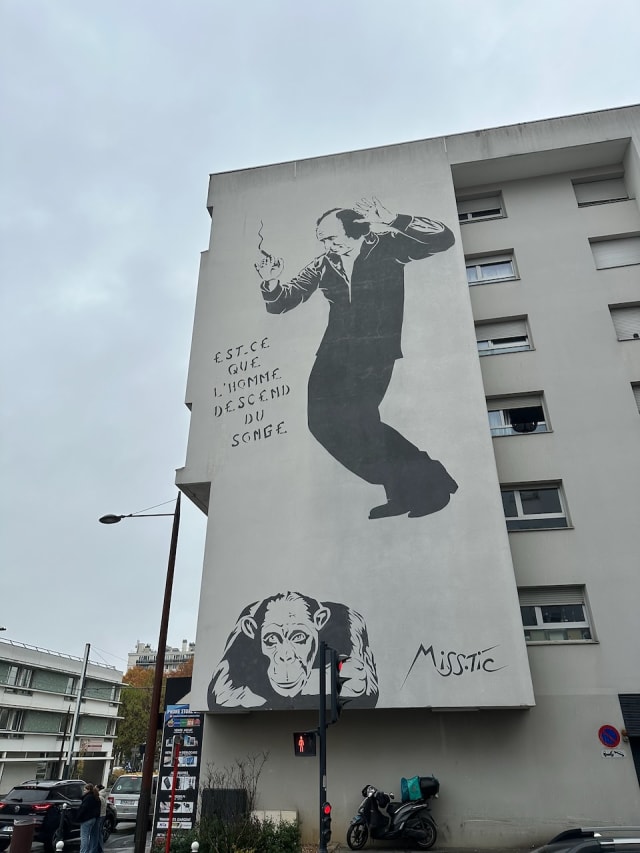 Un dessin de Miss-Tic sur un mur d'immeuble avec un homme qui danse et un chimpanzé les bras croisés, avec le texte « Est-ce que l'homme descend du songe »