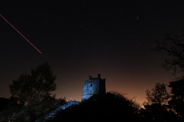 Photo des étoiles avec la Tour Denecourt au premier plan, et la trace d'un avion qui passe