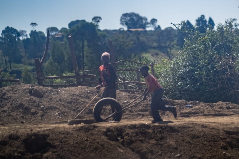 Slightly blurred photo of two Kenyan children playing by rolling a tire with sticks