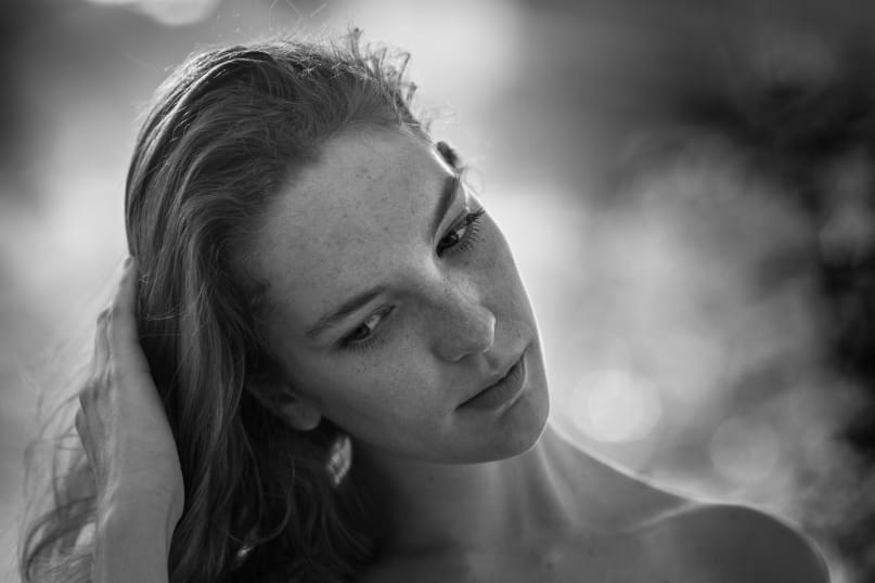 Tight black and white portrait of a young woman, her head tilted to the side, her hand in her hair