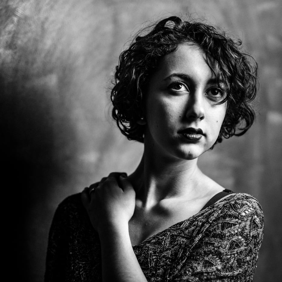 Contrasting black and white portrait of a young woman with curly hair, in front of a wall