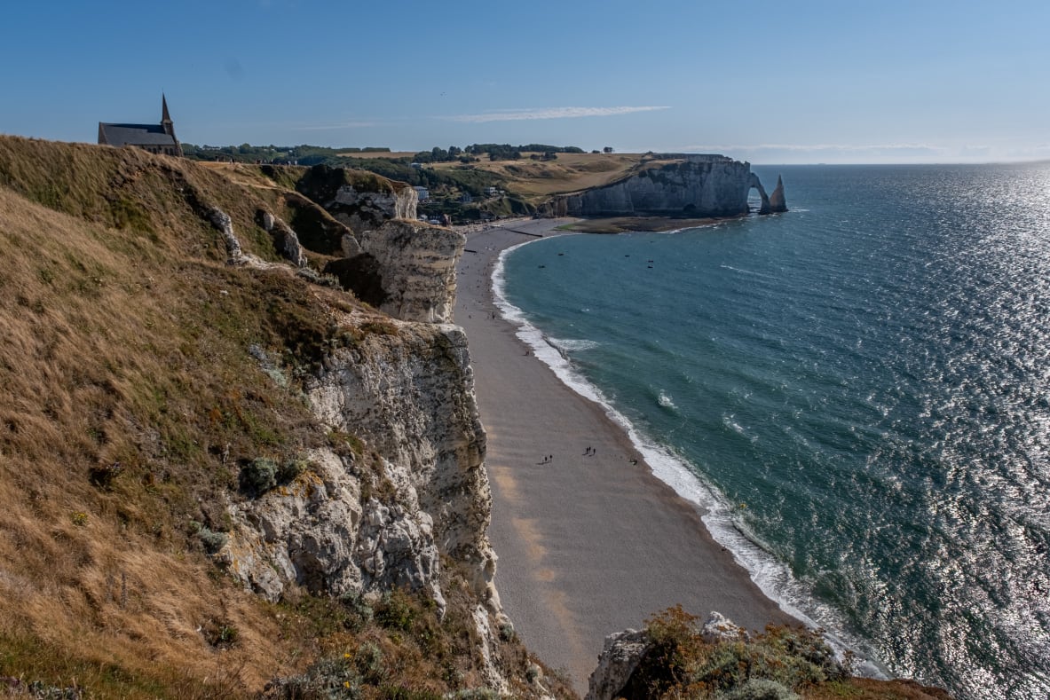 A panoramic view of a coastal landscape featuring white cliffs with an arch, and a beach.